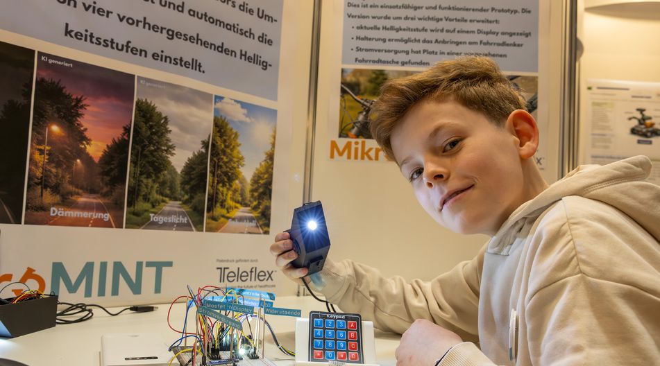 Junge hält eine leuchtende elektronische Schaltung mit Sensor und Tastenfeld auf einer Messe.