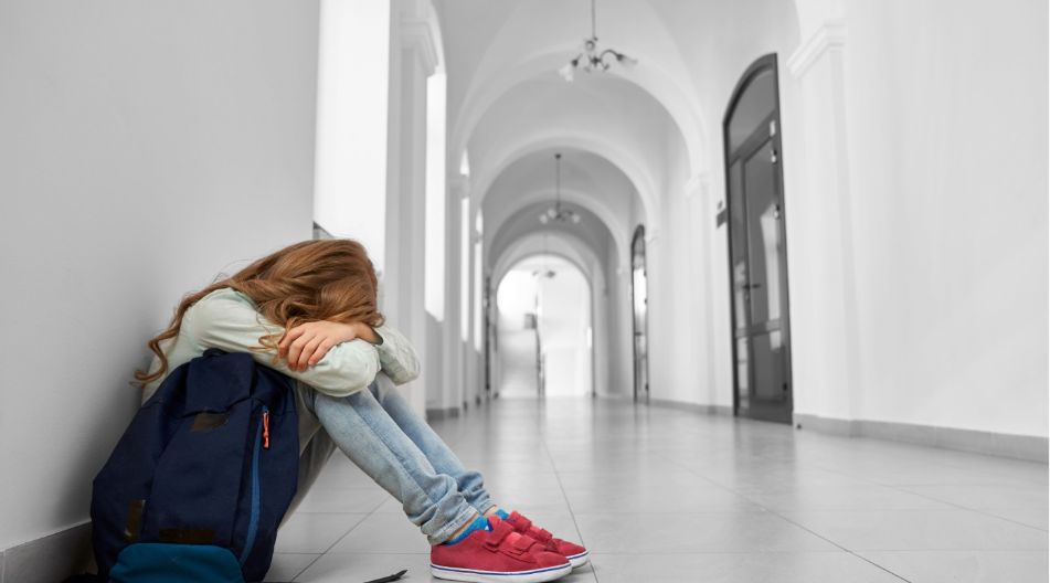 Ein Mädchen sitzt zusammengesunken auf dem Schulflur und vergräbt ihr Gesicht.