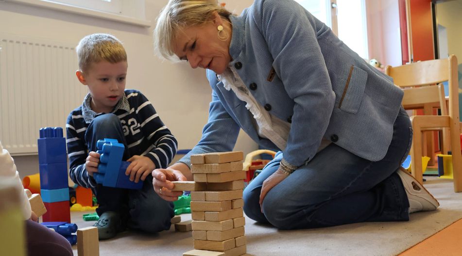 Bildungsministerin Simone Oldenburg und ein Kind der Kita Seestern knien auf dem Boden. Sie bauen gemeinsam mit Holz- und Kunststoffbausteinen einen Turm.