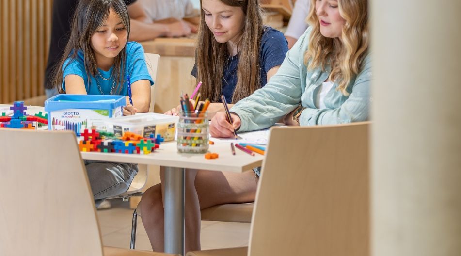 Kinder sitzen in einer Kita an einem Tisch und malen zusammen in einem kreativ gestalteten Raum. Kinder sitzen in einer Kita an einem Tisch und malen zusammen in einem kreativ gestalteten Raum.